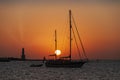 Red sky in a sunset over the sea, the silhouettes of a lighthouse and sailboats.