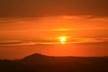 Red sky and the yellow sun with cloud lines and the hills in foreground