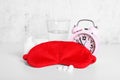 Red sleep mask, glass of water, pills and alarm clock on white table Royalty Free Stock Photo