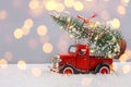 Red small retro toy truck with sparkling Christmas tree lights on truck body on blurred background with bokeh. Royalty Free Stock Photo