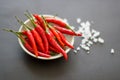 Red small spicy peppers in a green bowl with salt crystals nearby on a black background.Close-up, top view