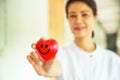 Red smiling heart held by smiling female nurse`s hand, representing giving effort high quality service mind to patient.