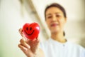 Red smiling heart held by smiling female nurse`s hand, representing giving effort high quality service mind to patient.