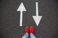 Red sneakers on the asphalt road with drawn arrows pointing to two directions