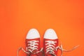 Red sneakers with untied laces with copy space. Youth sneakers on an orange background. Top view, flat lay