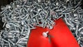 Red spatula picking up metal stainless steel screws.Shiny short self-tapping screws close-up. Warehouse of small parts for the