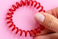 Red spiral rubber bands for hair hold fingers with pink manicure of a young woman on a pink background close-up Royalty Free Stock Photo