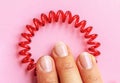 Red spiral rubber bands for hair hold three fingers with pink manicure of a young woman on a pink background close-up Royalty Free Stock Photo