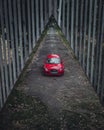 red sports car parked on a dirt path next to tall wooden fence