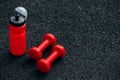 Red sports water bottle and sports dumbbells on a black rubberized sports field, background image