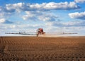 red sprayer with long arms at the arable field makes fertilizers in early spring view with clouds Royalty Free Stock Photo