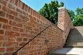 Red staircase descends under the terrain of a grassy yard with park paths. the walls are made of machined brick blocks and concret