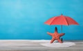 Red starfish and beach umbrella on the white sand and rustic table over blue background Royalty Free Stock Photo