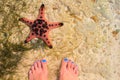 Red starfish and woman in sea water. Seaside with white sand. Sea sand top view with female feet. Royalty Free Stock Photo