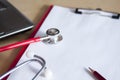 Red stethoscope and red pencil on a red clipboard on a table. Near laptop. Medical device. Treatment, health care. Heart