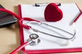 Red stethoscope, red pencil and heart on a red clipboard. Near laptop. Medical device. Treatment, health care. Heart examination.