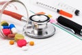 Red stethoscope, syringes, pen, and many colorful pills on blank notepad Royalty Free Stock Photo