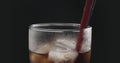 Red straw in cola with ice cubes in glass over black background