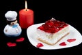 Red strawberry cake on white plate, candle, hearts and toy cook isolated on black background.  Holiday food for Valentine day, Royalty Free Stock Photo