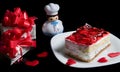 Red strawberry cake on white plate, hearts, gift box and toy cook isolated on black background.  Holiday food for Valentine day Royalty Free Stock Photo