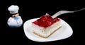 Red strawberry cake on white plate and toy cook isolated on black background. Holiday food Royalty Free Stock Photo