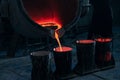 A red stream of molten metal pours into the mold from a large vat