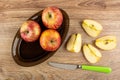 Red apples in oval dish, slices of apple, table knife on wooden table. Top view