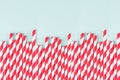 Red striped cocktail straws on pastel mint color as abstract joyful background, border with copy space.