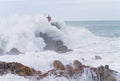 Red structure of beacon on North Rock ar base of Mount Maunganui with wild stormy sea crashing around and over it