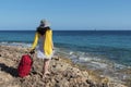 Red suitcase and fancy dress. Curly Caucasian woman on a coast Royalty Free Stock Photo