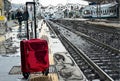 A red suitcase in the train station, near the tracks