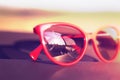 Red sunglasses on the car dashboard with reflection of the sun.