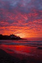 Red sunset at the beach with town in silhouette and dramatic sky with clouds. Amazing sunlight sunrise seascape with waves and Royalty Free Stock Photo