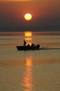 Red sunset on the still sea, black silhouette of boat with three men fishing Royalty Free Stock Photo