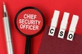 On the red surface lies a pen, a notebook with clothespins - CSO, and a magnifying glass - Chief Security Officer