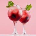 Red sweet cold party drinks in two elegant wineglasses with ice cubes, blueberry, green mint on pastel soft pink color background.