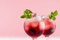 Red sweet cold party drinks in two elegant wineglasses with ice cubes, blueberry, green mint on pastel soft pink color background.