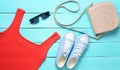 Red T-shirt, sneakers, leather bag, sunglasses on a blue wooden table. Women& x27;s clothing, footwear and accessories, top view Royalty Free Stock Photo