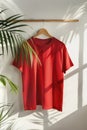 Red t-shirt on wooden hanger against a white wall with plant shadows