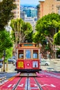 Red and tan streetcar 11 on uphill incline with sunny green sycamore trees behind it, San Francisco, CA