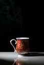 A red tea cup with designs on it placed on a white reflective table and smokes of hot tea coming out of it Royalty Free Stock Photo