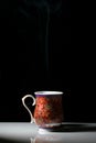 A red tea cup with designs on it placed on a white reflective table and smokes of hot tea coming out of it Royalty Free Stock Photo