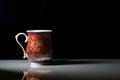 A red tea cup with designs on it placed on a white reflective table and smokes of hot tea coming out of it. Landscape view Royalty Free Stock Photo