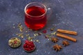 Red tea rooibos, hibiscus, karkade in glass cup and teapot among cinnamon, anise, cranberries on a dark background. Herbal, Royalty Free Stock Photo