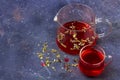 Red tea rooibos, hibiscus, karkade in glass cup and teapot among dry tea leaf, petals and cranberries on a dark background. Royalty Free Stock Photo