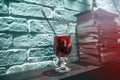 Red tea in a tall glass cup against a brick wall and a stack of books in red-blue backlight Royalty Free Stock Photo