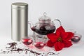 Red tea in teapot on stand with candle, glass cups, stainless container, scattered dry herbs and poinsettia flower on Royalty Free Stock Photo