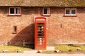 Red telephone booth near a brick wall with windows Royalty Free Stock Photo