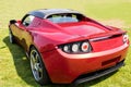 Red Tesla Roadster Sports Car Rear Side in Green Field