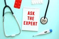 The red text ASK THE EXPERT is written on a white notepad that lies next to the stethoscope on a blue background. Royalty Free Stock Photo